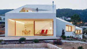 Fachada blanca de una casa verdaderamente sostenible con grandes ventanales y diseño bioclimático en entorno natural