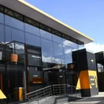 Motorhome del equipo McLaren de Fórmula 1 en el paddock de un circuito europeo, con diseño moderno, cristal templado y colores corporativos