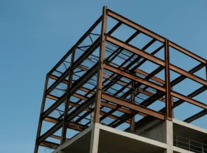 Vista de una obra en construcción con estructura metálica expuesta en plantas superiores y niveles inferiores ejecutados en hormigón armado, con grúa torre al fondo