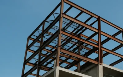 Vista de una obra en construcción con estructura metálica expuesta en plantas superiores y niveles inferiores ejecutados en hormigón armado, con grúa torre al fondo