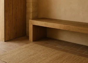 Banco de madera apoyado en pared de yeso natural y muro de piedra sobre suelo de barro cocido y alfombra de yute