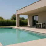 Piscina rectangular junto a terraza cubierta de una casa moderna, rodeada de vegetación