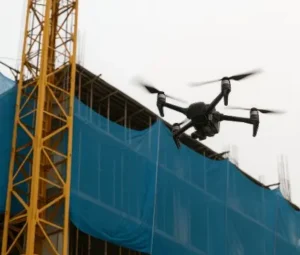 Dron sobrevolando un edificio en construcción con redes de protección azules y grúa torre amarilla. Preguntar a ChatGPT
