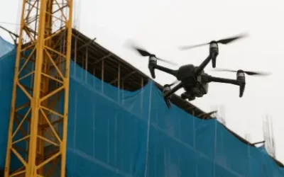 Dron sobrevolando un edificio en construcción con redes de protección azules y grúa torre amarilla. Preguntar a ChatGPT