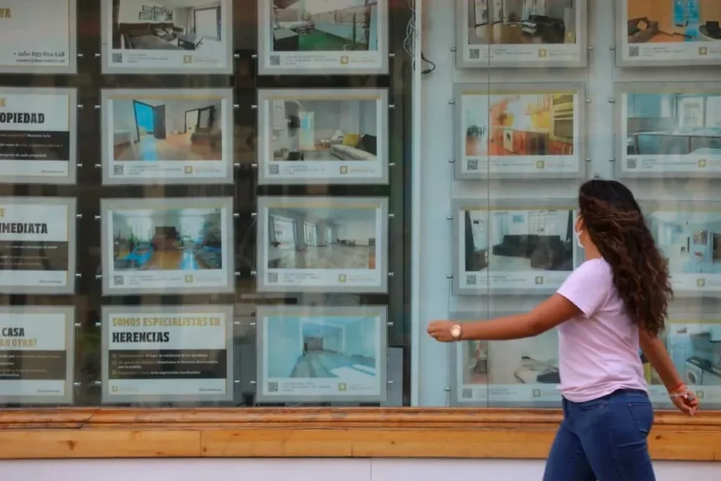 Mujer mirando escaparate inmobiliario relacionado con control del alquiler y oferta de viviendas