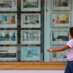 Mujer mirando escaparate inmobiliario relacionado con control del alquiler y oferta de viviendas