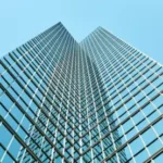 Fachada de vidrio laminado y estructura metálica reflejando el cielo en un edificio contemporáneo, símbolo de arquitectura sostenible y eficiente.