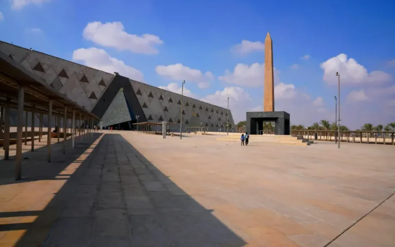 Vista panorámica del Gran Museo Egipcio con su fachada de alabastro y el obelisco de entrada bajo un cielo azul despejado en Giza, Egipto