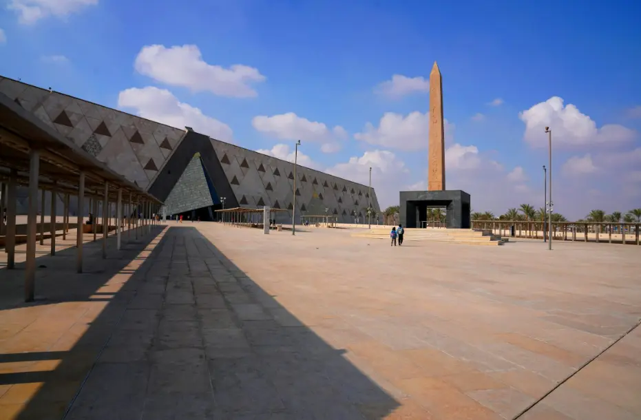 Vista panorámica del Gran Museo Egipcio con su fachada de alabastro y el obelisco de entrada bajo un cielo azul despejado en Giza, Egipto