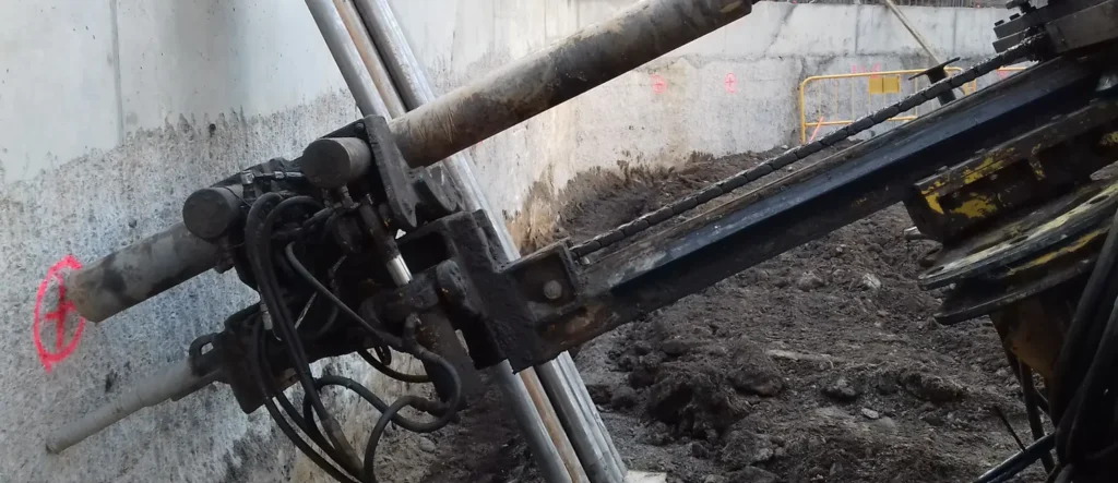 Equipo perforador realizando taladros inclinados para anclajes en un muro pantalla durante una excavación