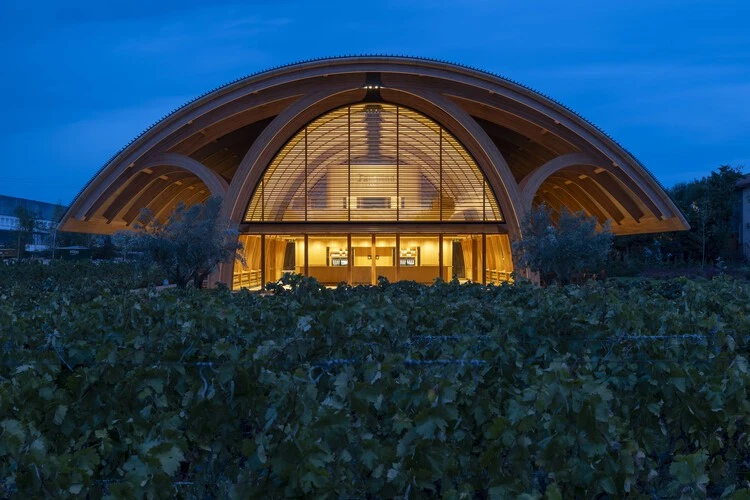 Arquitectura de bodegas con estructura de madera curva e iluminación cálida en Faustino.