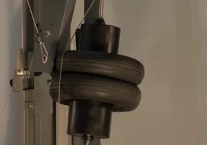 Péndulo de doble neumático negro suspendido sobre soporte gris oscuro durante un ensayo de impacto pendular en vidrio de seguridad en laboratorio técnico.